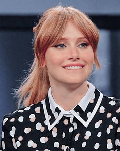 a woman with red hair wearing a black and white polka dot shirt smiles at the camera