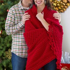 a man and woman wrapped in a red shawl by a christmas tree with presents