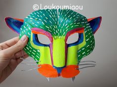 a hand holding up a paper mask with an animal's face painted on it