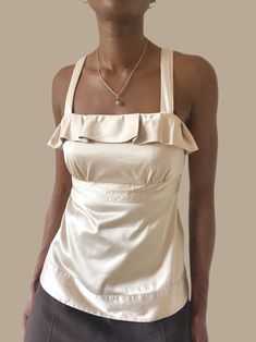 "Vintage Champagne Ruffle Trim Satin Sleeveless Belted Blouse MEASUREMENTS  Size: S Pit to Pit: 15.5\" IN Bust: 29\" IN Length: 23.5\" IN Model wears a 4  MATERIAL 96% Polyester, 4% Spandex All purchases are non refundable. You are purchasing a one of one item. Please read all information provided about an item. All sales are final" Fitted Sleeveless Solid Color Blouse, Feminine Camisole Top, Fitted Ruffled Tank Camisole, Fitted Ruffle Camisole Top, Fitted Ruffle Tank Camisole, Fitted Ruffled Cami Top, Beige Camisole Top For Party, Beige Tank Top For Party, Fitted Ruffled Sleeveless Tank Top