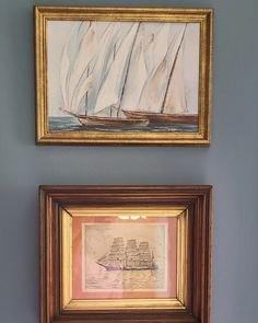 two framed paintings on the wall above each other, one with a sailboat painted on it