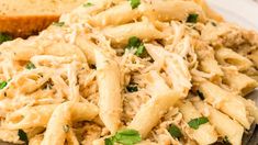 pasta with chicken and parmesan cheese is served on a white plate next to bread