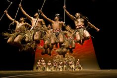 a group of men standing on top of a stage holding onto sticks and wearing headdress