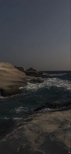 an airplane is flying over the ocean with waves crashing on it's shore and rocks in the foreground