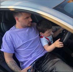 a man sitting in the driver's seat of a car holding a small boy