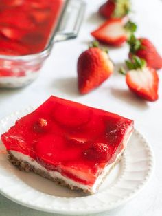 a piece of strawberry cheesecake on a white plate with strawberries in the background