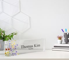 a clear acrylic sign sitting on top of a desk next to a potted plant