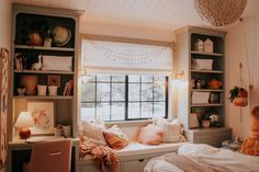 a window seat with pillows and blankets on it in front of a bookcase filled with books