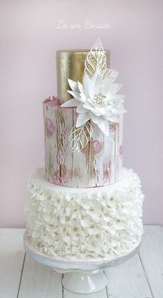 a three tiered cake with white flowers and lace on the top, sitting on a pedestal