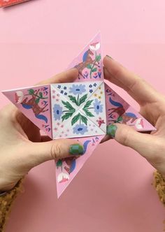 someone is holding up a paper origami star on a pink surface with other items