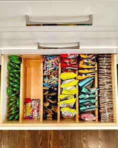 an organized kitchen drawer filled with snacks and candy bar wrappers, on top of wood planks