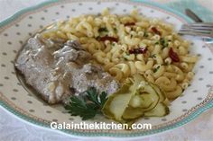 a white plate topped with pasta and meat covered in gravy next to veggies