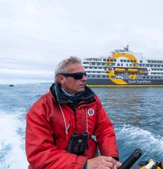 a man on a boat in front of a large cruise ship with the ocean behind him