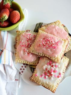 strawberry shortbreads with frosting and sprinkles on a plate next to a bowl of strawberries