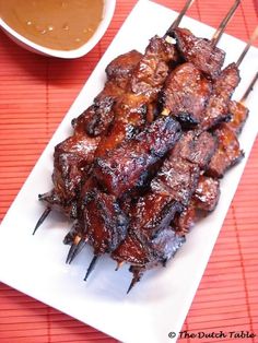 several skewers of meat on a plate with dipping sauce