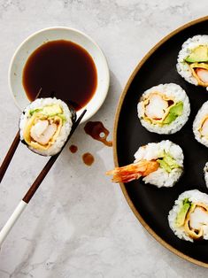 sushi on a black plate with chopsticks next to it and dipping sauce