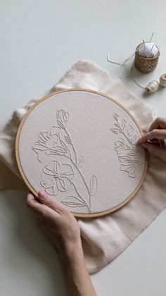 a woman is working on an embroidery project with her hands and needle in the background