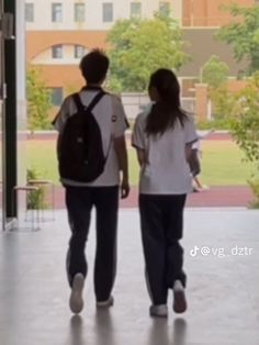 two people walking in an open building with their back to the camera and one person carrying a backpack