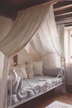 a canopy bed with white curtains and pillows