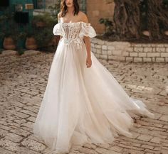 a woman in a white wedding dress standing on a cobblestone street