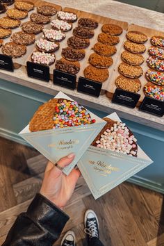 a person holding up two cards with different types of cookies on them in front of a display case