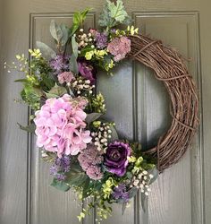 a wreath with purple flowers and greenery hanging on a door