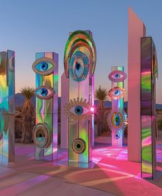 an array of metal sculptures with eyes on them in front of palm trees and sky