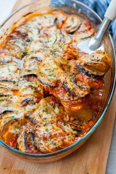 a casserole dish with zucchini and tomato sauce in it on a wooden cutting board