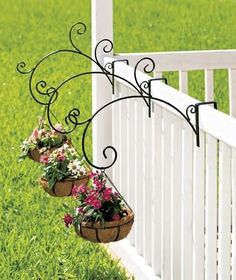 three flower pots hanging from the side of a white fence with green grass in the background