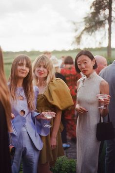 three women standing next to each other in front of a group of people holding plates