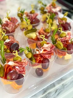 small cups filled with different types of food on top of a glass table covered in cheese and olives