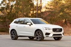 a white volvo suv parked in front of some trees