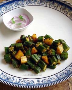 a white plate topped with green vegetables next to a small bowl filled with red onions