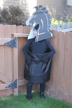 a person in a horse costume standing next to a fence with a horse head on it's back