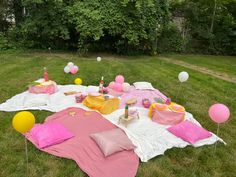 an outdoor picnic with balloons, cake and other items laid out on the grass in front of trees