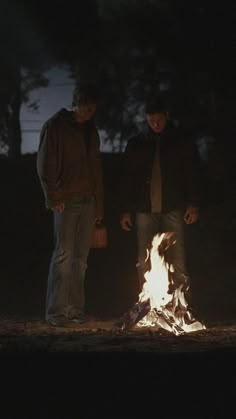 two men standing around a campfire at night