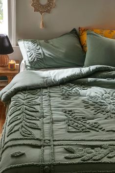 a bed with green comforter and pillows in a bedroom next to a lamp on a table