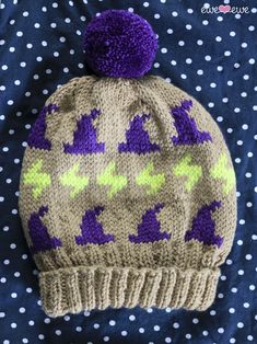 a knitted beanie with purple and green designs on the front, sitting on top of a polka dot blanket