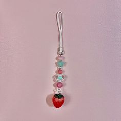 a red strawberry hanging from a hook on a pink wall with beads and charms attached to it