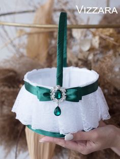 a hand holding a white and green basket with a ring on it's side