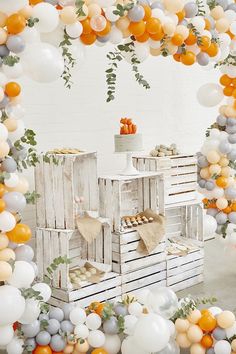 an orange, white and grey balloon arch with balloons around it in the shape of crates