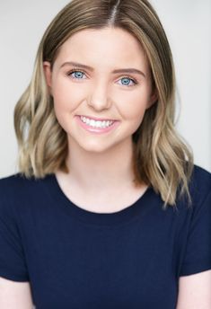 a woman with blonde hair and blue eyes smiles at the camera while standing in front of a white wall