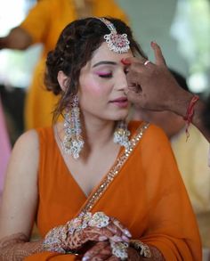 a woman in an orange sari getting her makeup done by a man with his hand on the forehead