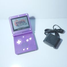 a purple nintendo gameboy sitting on top of a table next to a charger