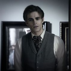 a young man wearing a vest and tie in a room with pictures on the wall