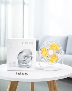 a white table with a yellow and white fan sitting on top of it next to a box