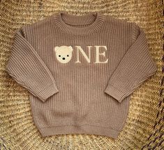 a brown sweater with a teddy bear on the front and one written in white across the chest