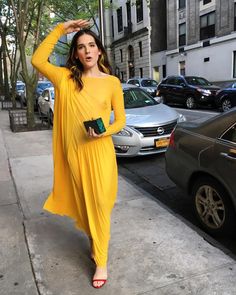 a woman in a yellow dress is standing on the sidewalk with her hands behind her head