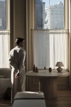 a woman standing in front of two windows looking out at the city outside her living room