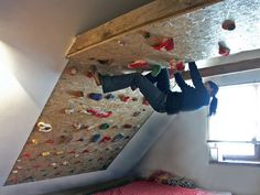 a man climbing up the side of a wall in a room with a bed and window